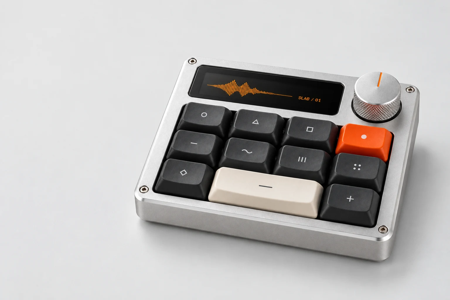 SLAB 01: a silver aluminium creative controller with charcoal keys, an ivory space key, orange accent key, and a knurled rotary dial.